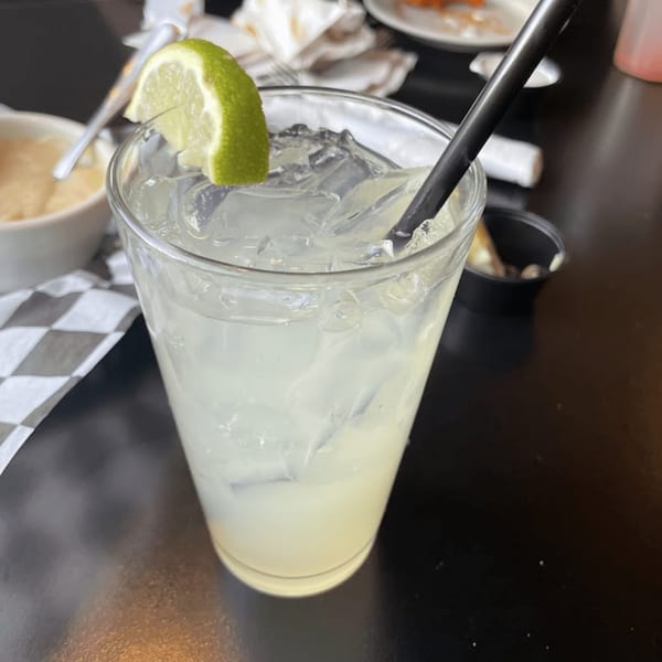 A glass of iced lemonade with a lime wedge and black straw on a dark table at Wild Duck Cafe.