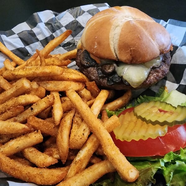 A Wild Duck Cafe mushroom swiss burger with seasoned fries, lettuce, tomato, and pickles.