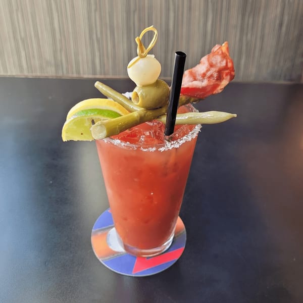A Bloody Mary cocktail garnished with olives, pickled green beans, lemon, lime, and bacon.