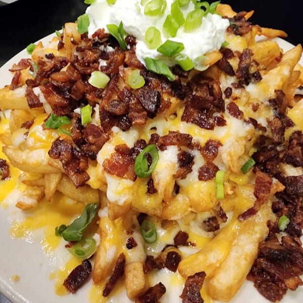 Loaded fries with melted cheese, crispy bacon bits, sour cream, and green onions on a white plate.