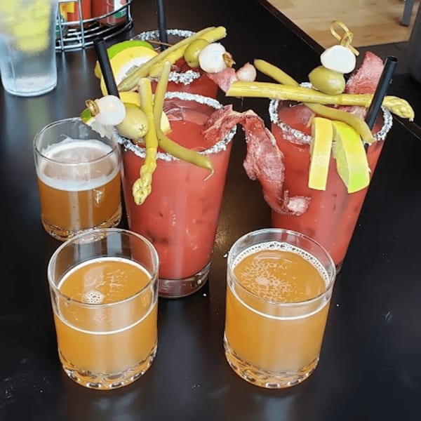Two Bloody Marys garnished with bacon, asparagus, and olives, alongside three glasses of beer.