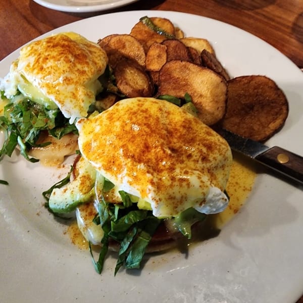 Wild Duck Cafe's Eggs Benedict with avocado, spinach, and crispy home fries on a white plate.
